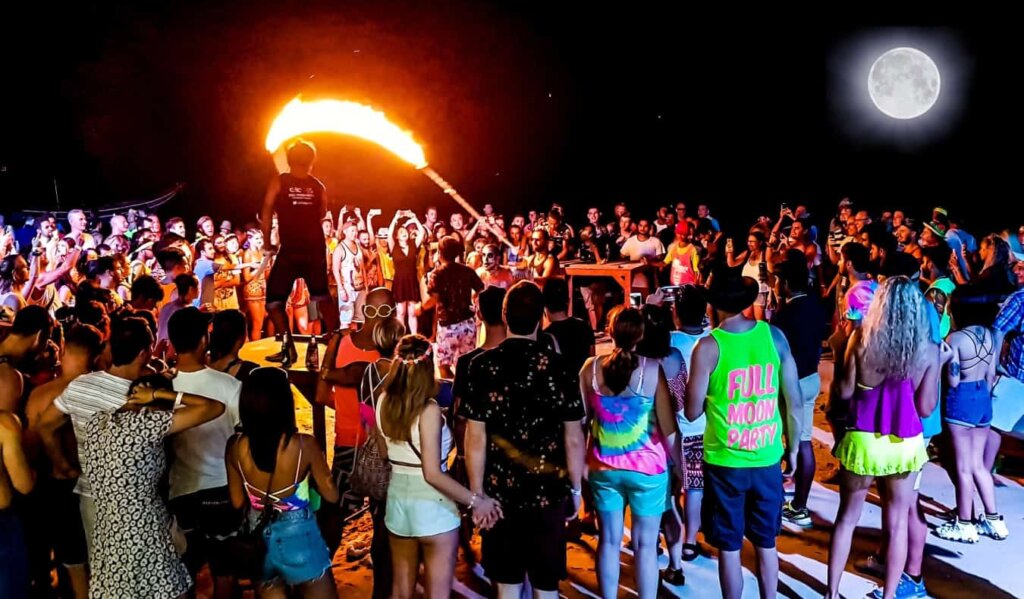 A crowd of people watch fire throwers at a beach in Thailand during the Full Moon Party