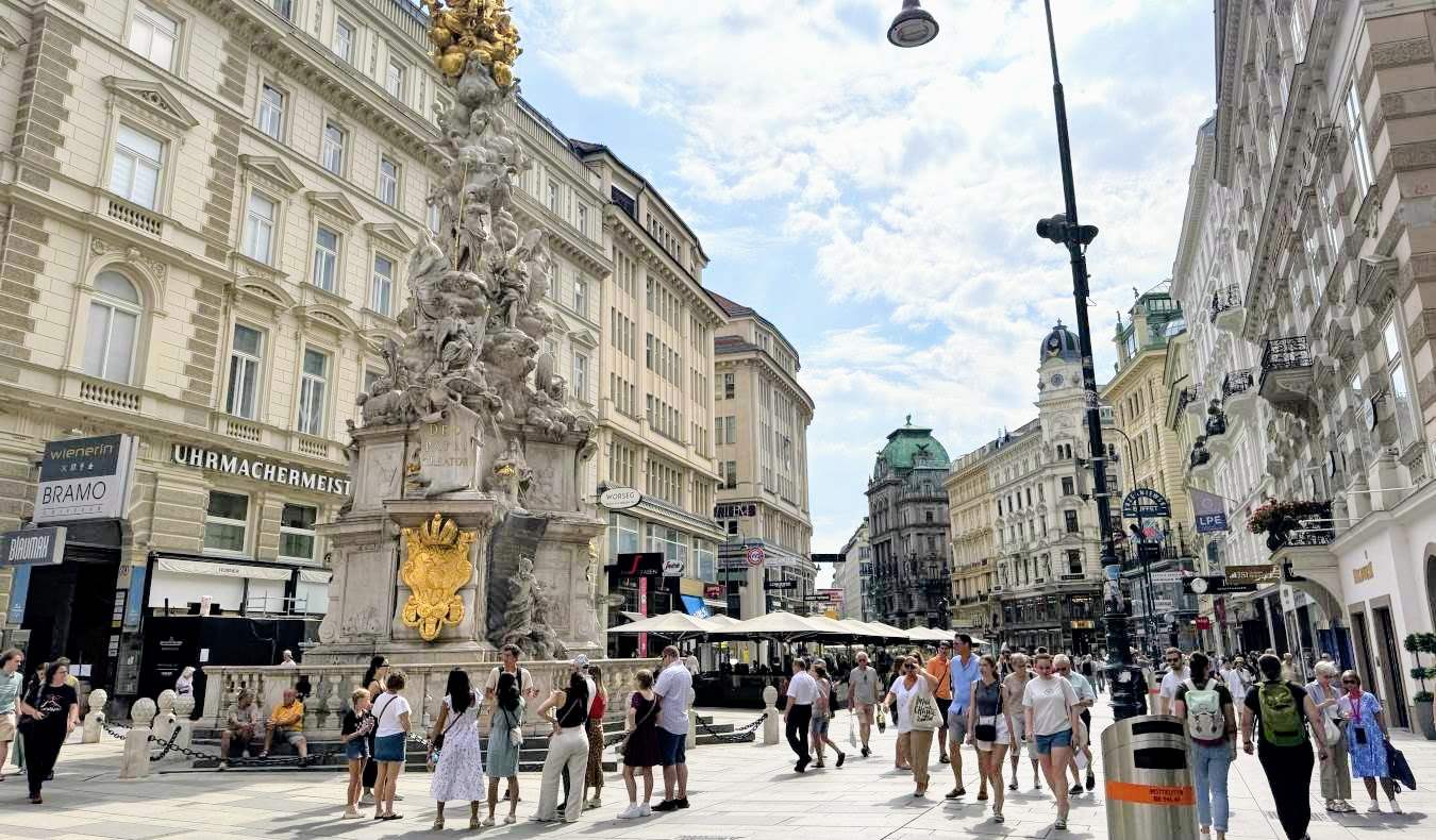 Crowds of people walk down a historic, pedestrianized street in downtown Vienna, Austria in the summer